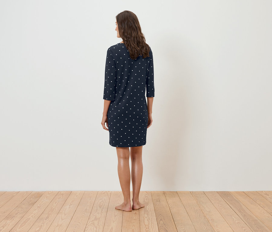 Une femme se tient dos à la caméra et porte une robe bleu marine à pois blancs.