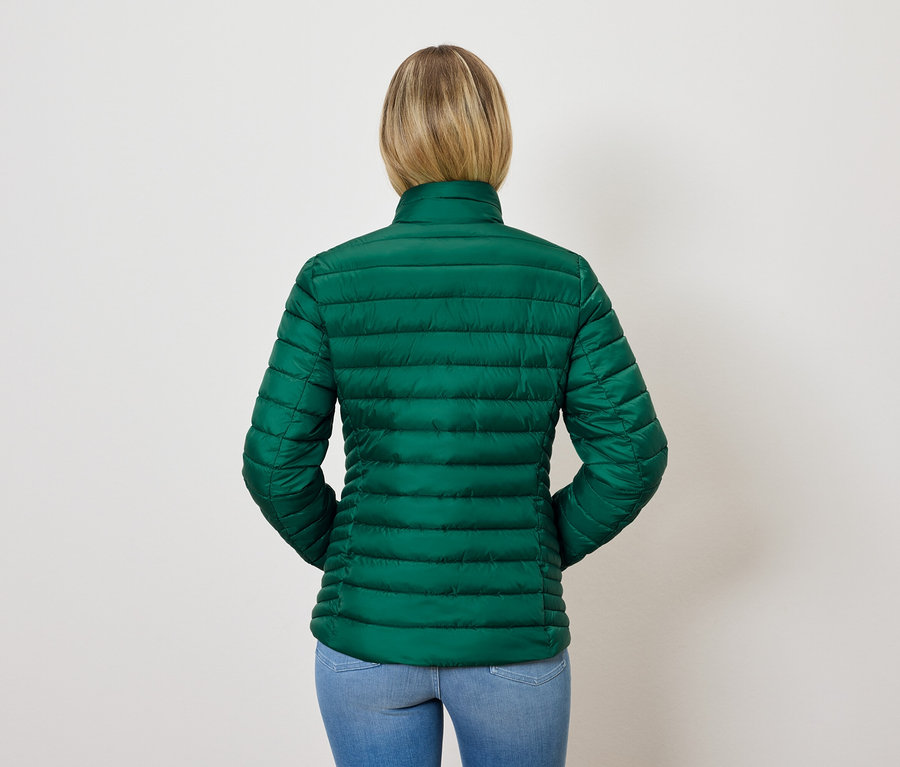 Vue arrière d'une femme aux cheveux blonds portant une veste matelassée verte et un jean bleu.