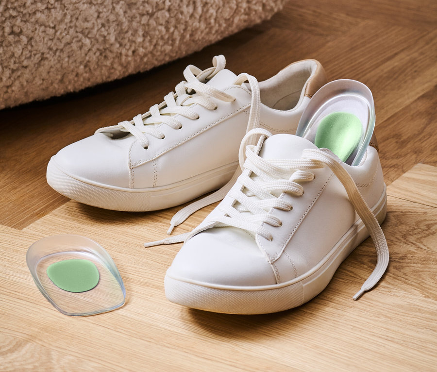 Deux baskets blanches sur un plancher en bois, dont une avec une semelle intérieure verte.