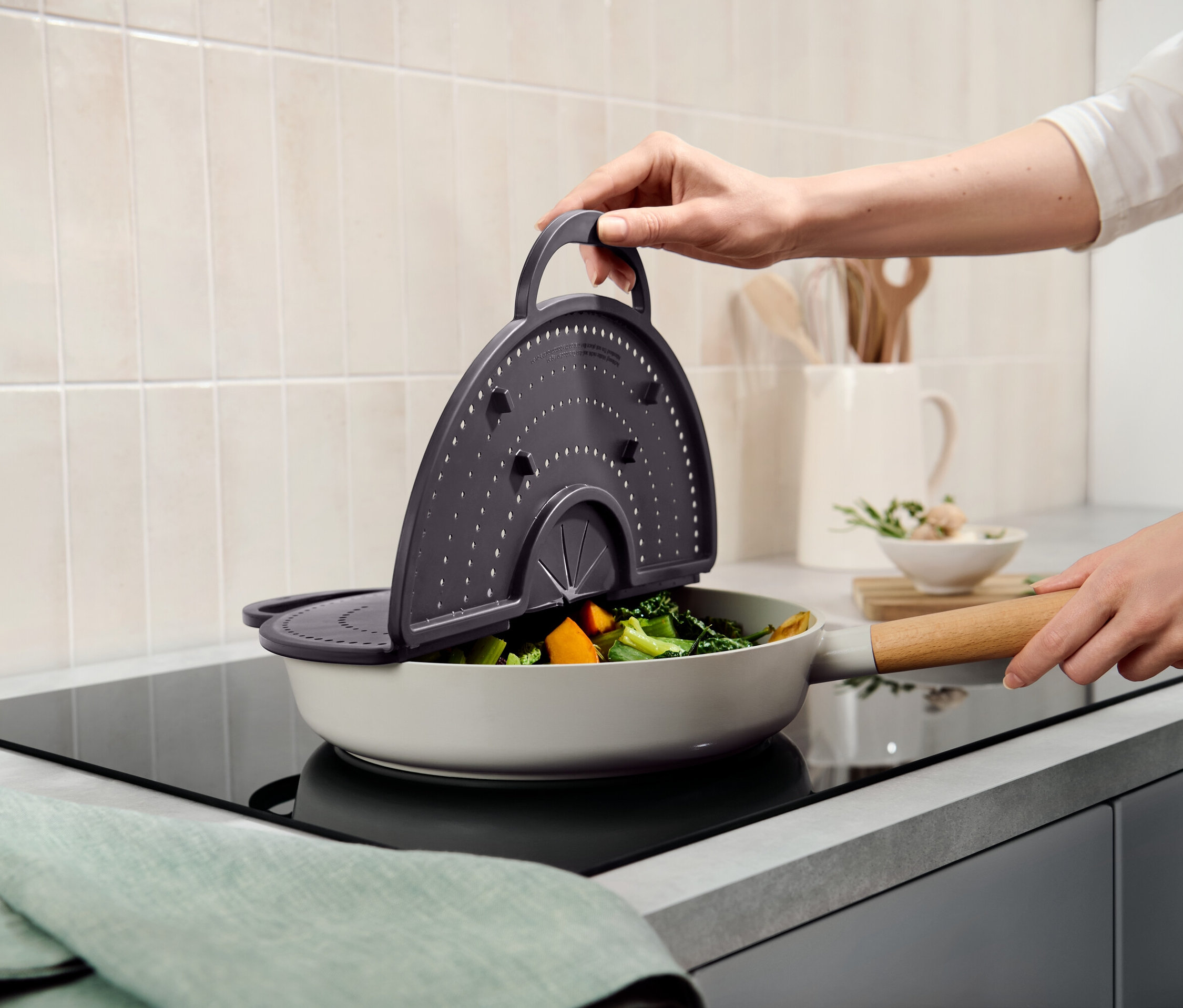 Une main tient une passoire grise au-dessus d'une poêle remplie de légumes.