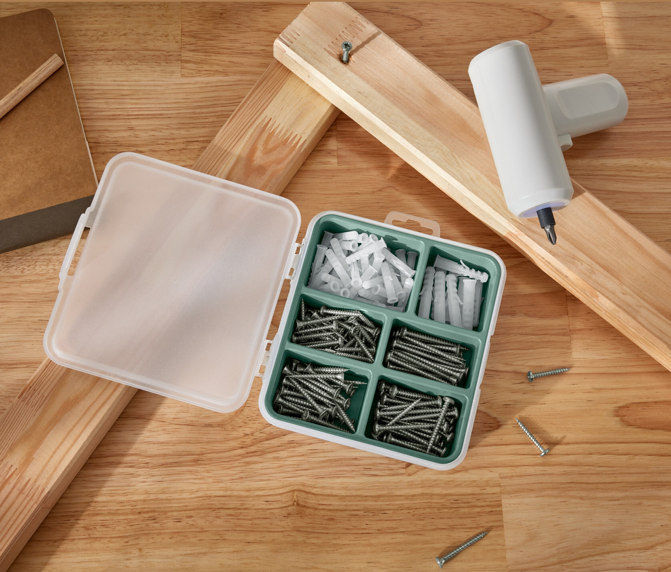 Un jeu de vis et de chevilles ouvert se trouve à côté de planches de bois et d'un tournevis sans fil.