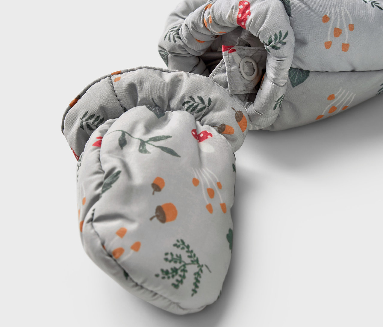 Gros plan sur une combinaison d’hiver pour bébé avec un motif de champignons, de glands et de brindilles.