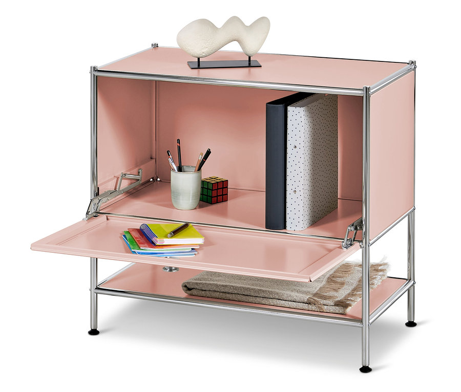 Armoire rose avec porte ouverte, à l'intérieur un gobelet avec des crayons, un cube et des classeurs, sur l'étagère inférieure une couverture et sur le dessus une sculpture.