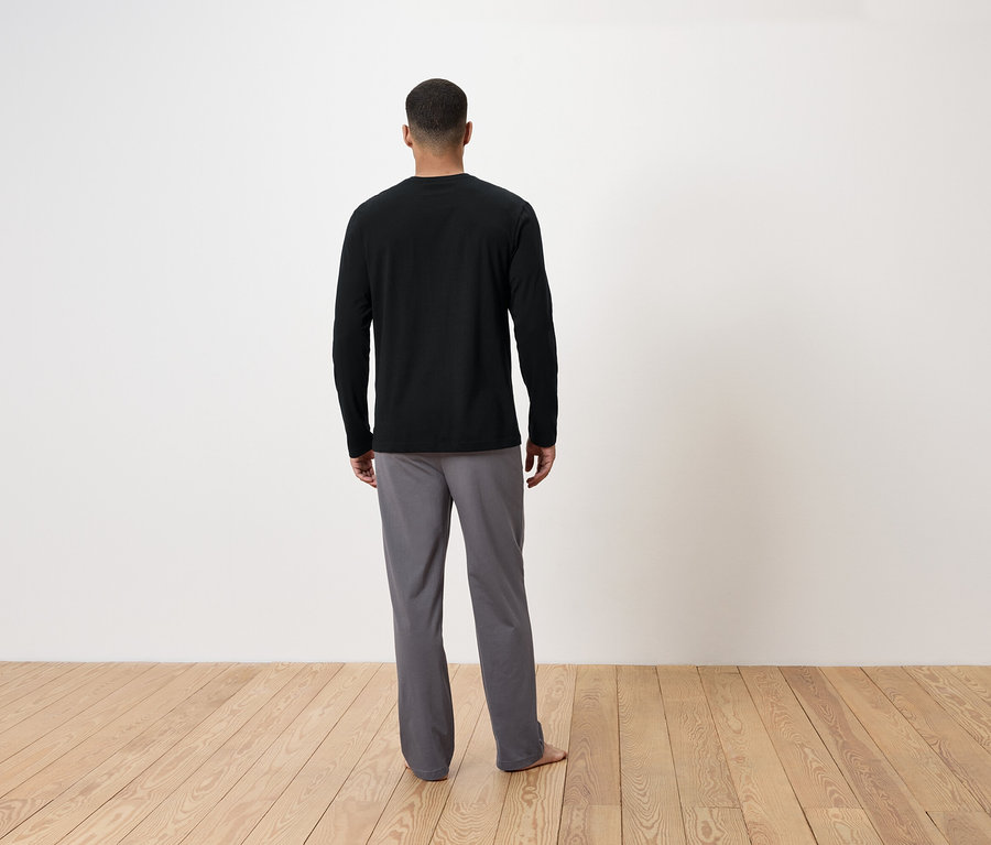 Un homme, vu de dos, porte un t-shirt noir à manches longues et un pantalon gris.