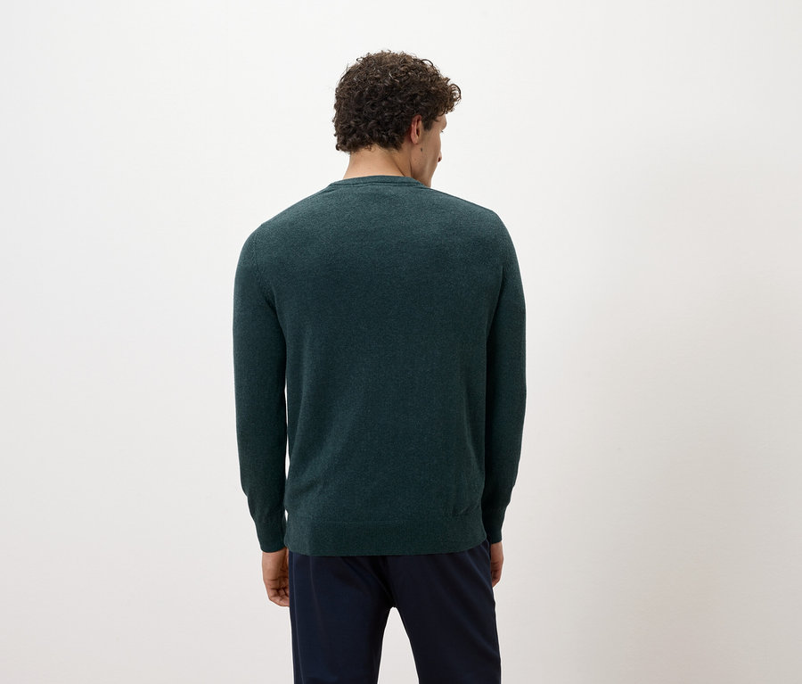 Un homme, dos à la caméra, porte un pull vert foncé et un pantalon bleu marine.