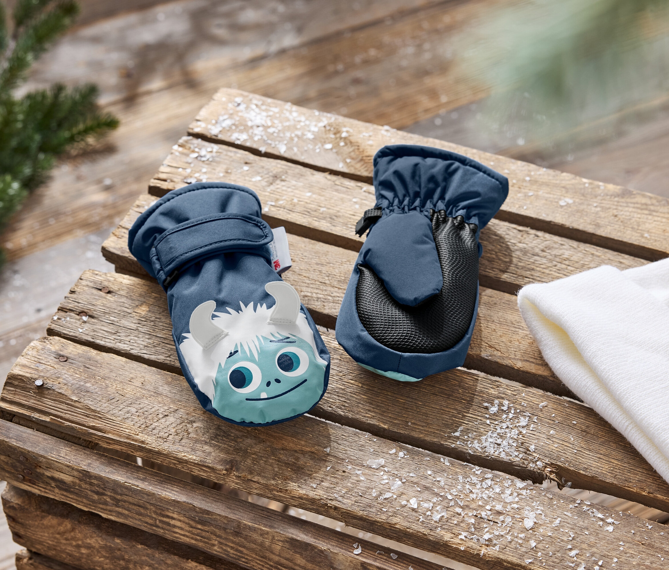 Deux moufles bleu marine pour enfants avec un imprimé bonhomme de neige sur un fond en bois.
