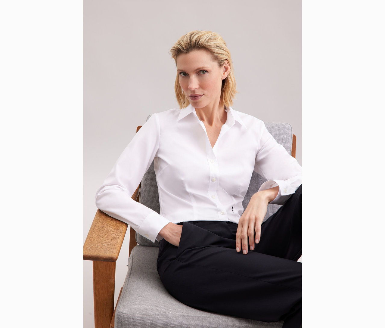 Femme assise sur une chaise portant un chemisier blanc Slim Fit non iron Seidensticker.