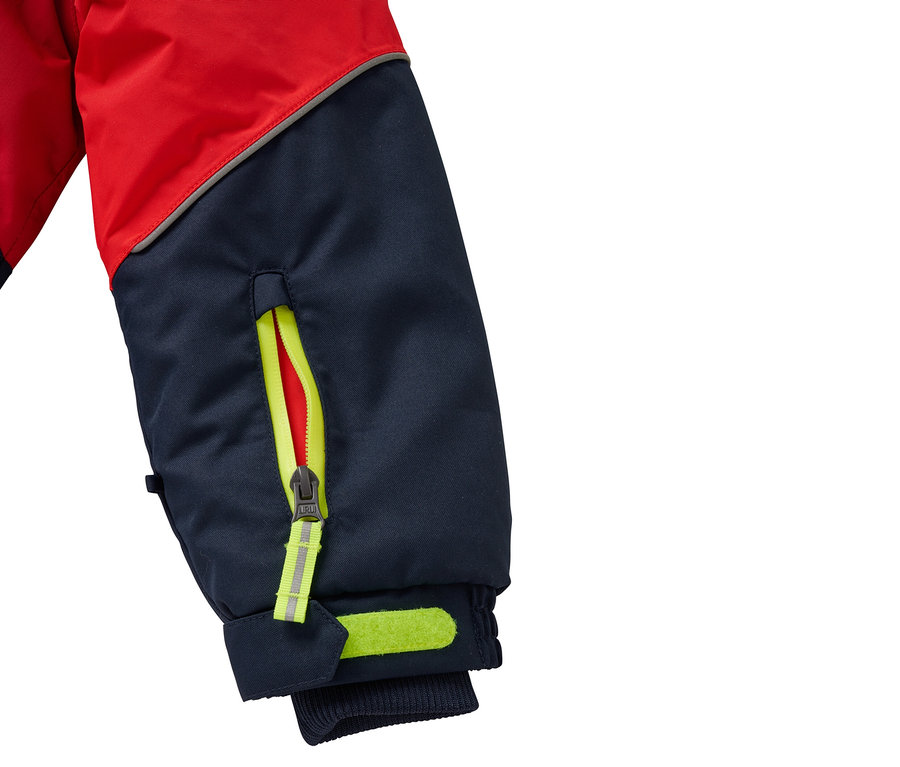Détail de la manche rouge et bleue d'une veste avec fermeture éclair jaune et éléments réfléchissants.