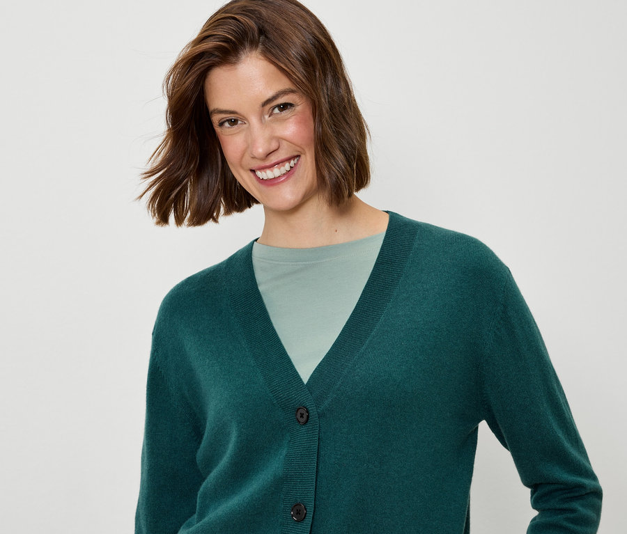 Une femme souriante aux cheveux bruns courts porte un cardigan vert et un t-shirt vert.