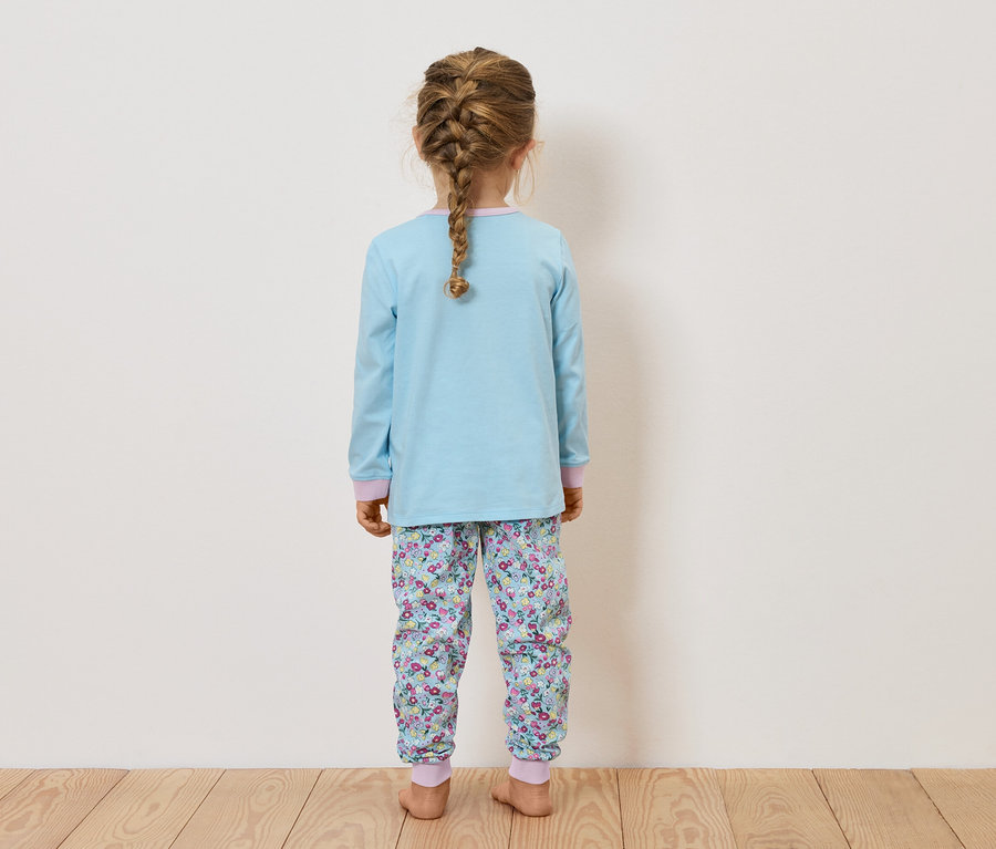 Une fille vue de dos, portant un pyjama bleu avec un pantalon à motifs floraux et les cheveux tressés.