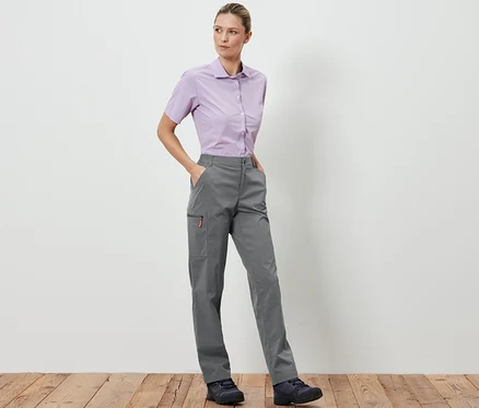 Une femme debout pose en pantalon outdoor pliable gris et une chemise violet clair.