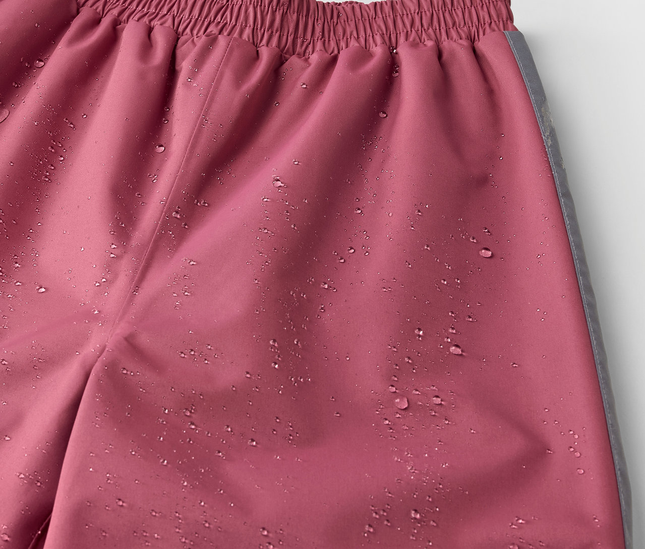 Gros plan sur un pantalon de pluie rose pour enfant avec des gouttes d'eau.
