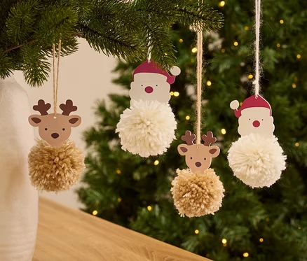 Des décorations de sapin de Noël avec des motifs de Père Noël et de renne et des pompons sont accrochées au sapin de Noël.