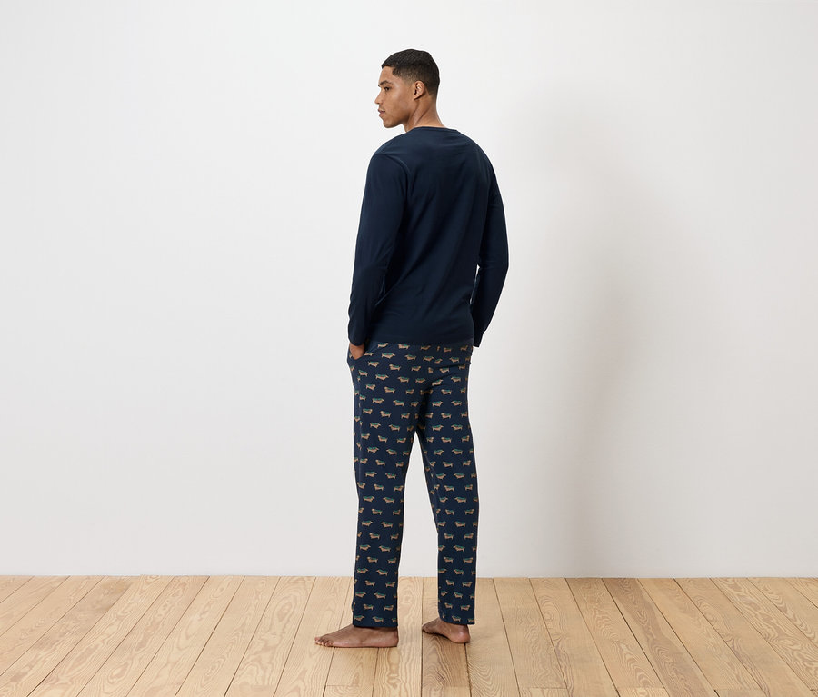 Un homme, vu de dos, porte un pyjama bleu marine avec un imprimé de teckels.