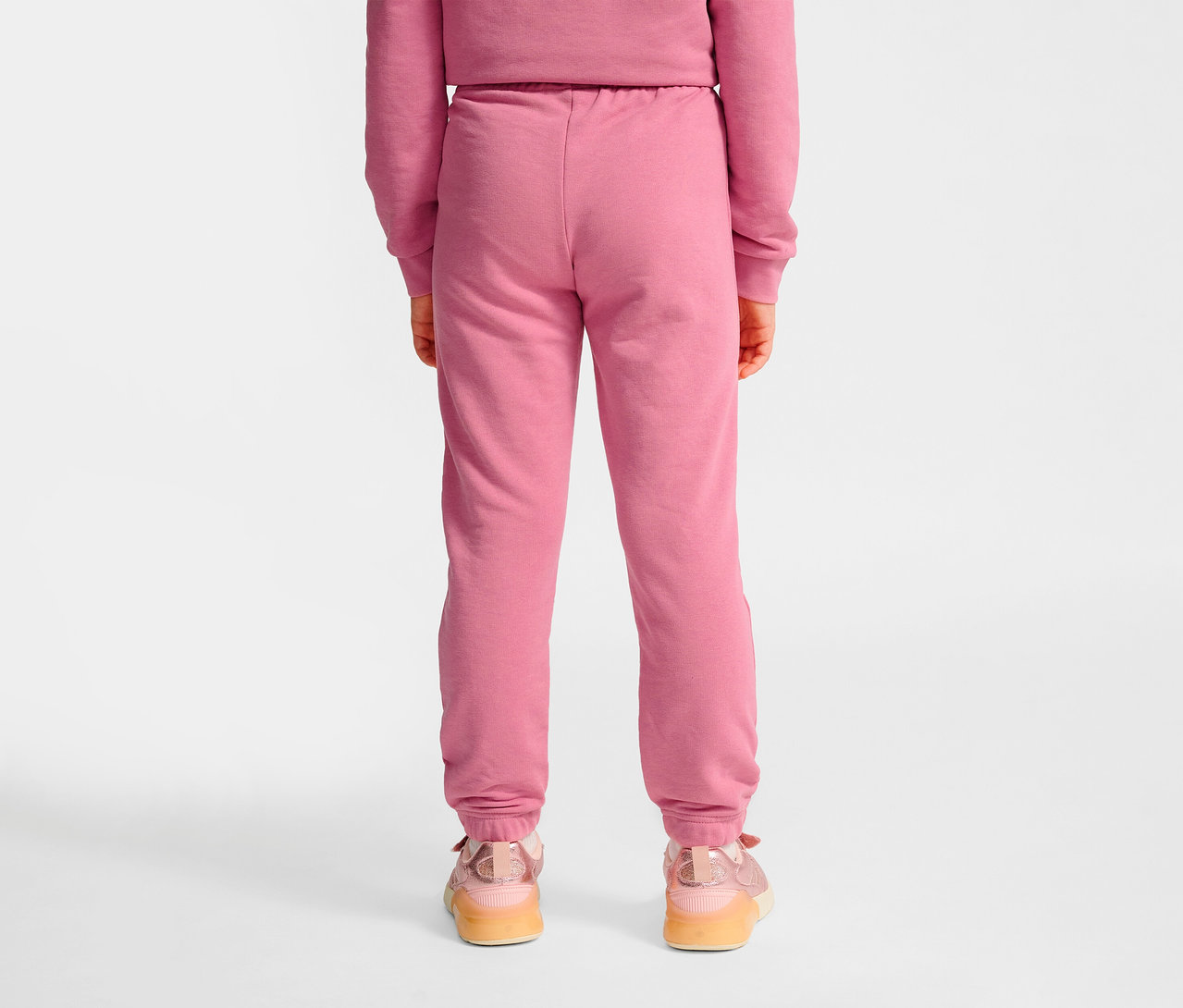 Vue arrière d'une fille portant un pantalon régulier HUMMEL HMLJR Base rose et des baskets.
