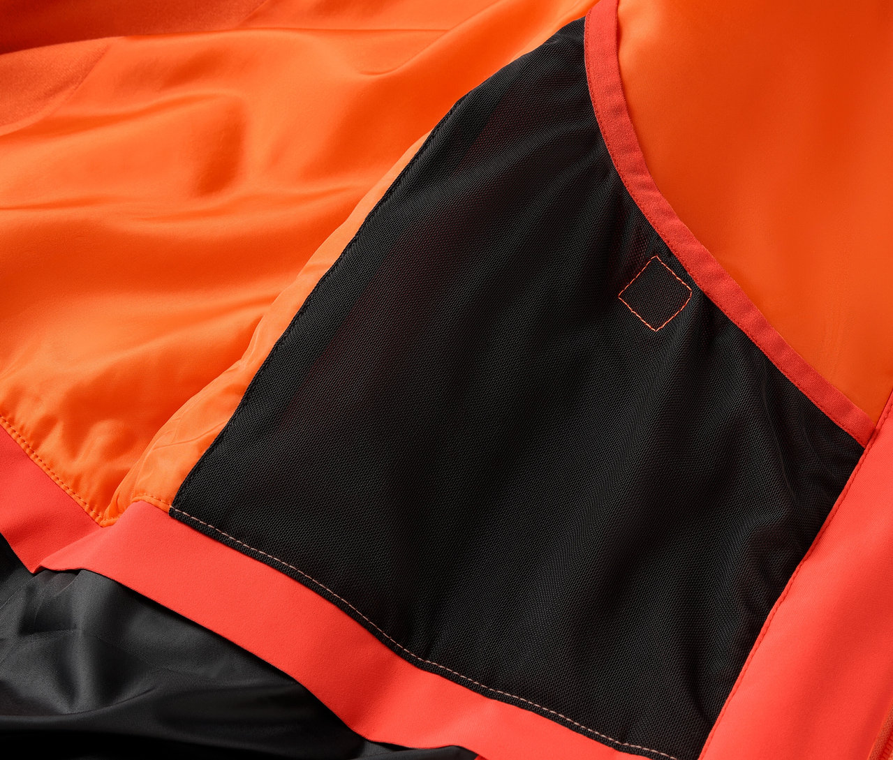 Détail d'une veste orange avec une poche noire.