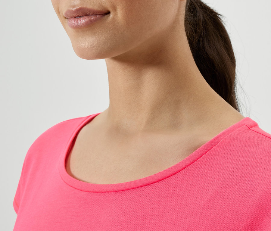Haut du corps d'une femme aux cheveux foncés attachés en queue de cheval, portant un t-shirt rose.