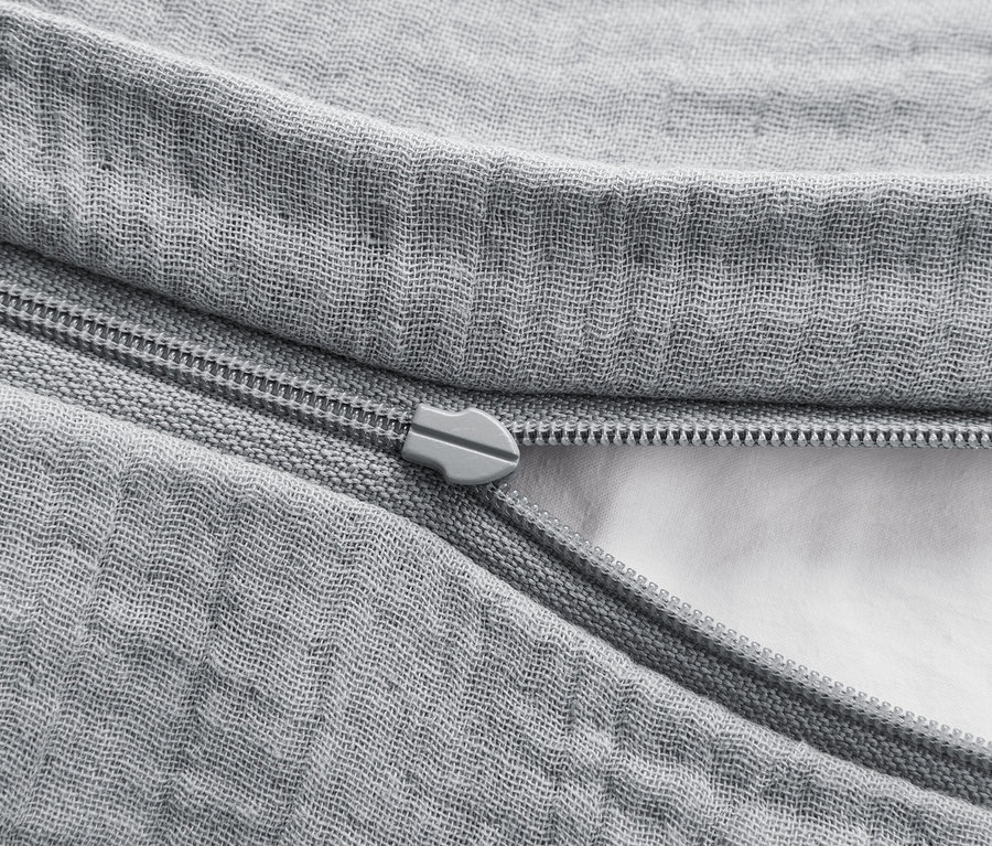 Gros plan d'une housse de couette grise avec une fermeture éclair partiellement ouverte, révélant un rembourrage blanc.