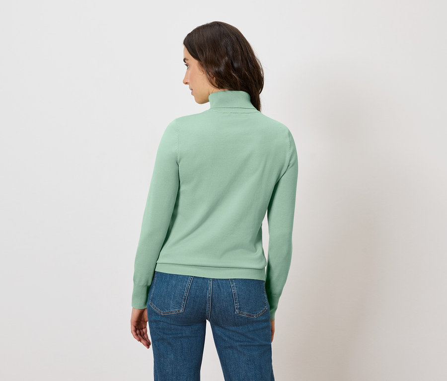 Une femme vue de dos porte un pull à col roulé vert clair et un jean.