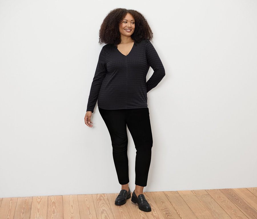 Une femme debout porte un t-shirt à manches longues structuré noir, un pantalon noir et des chaussures noires.