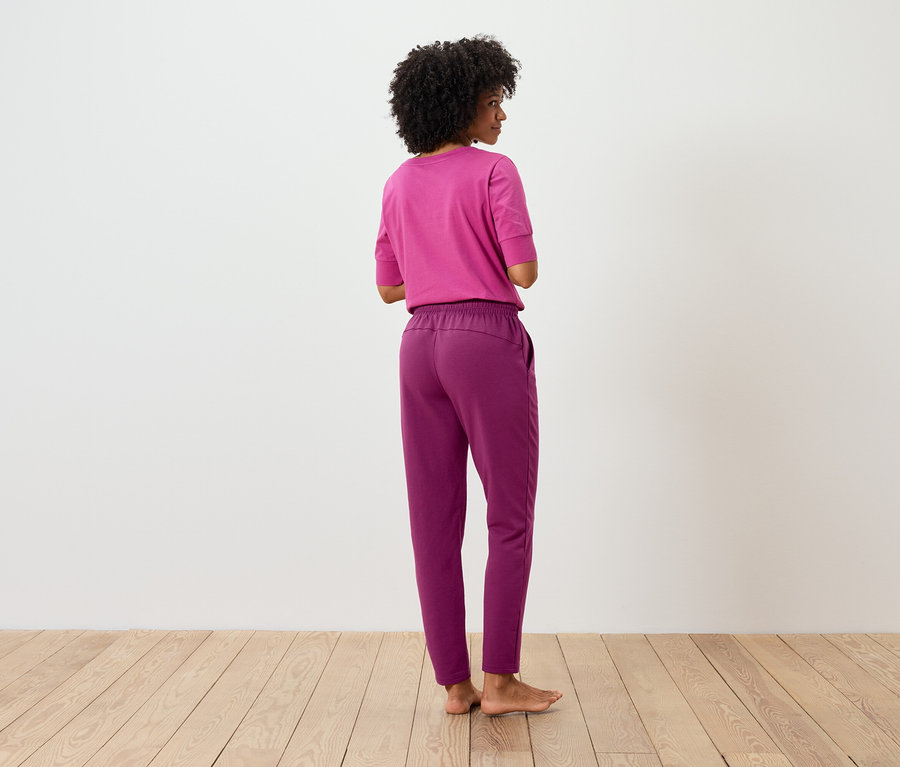 Femme afro, dos tourné, portant un t-shirt rose et un pantalon violet.