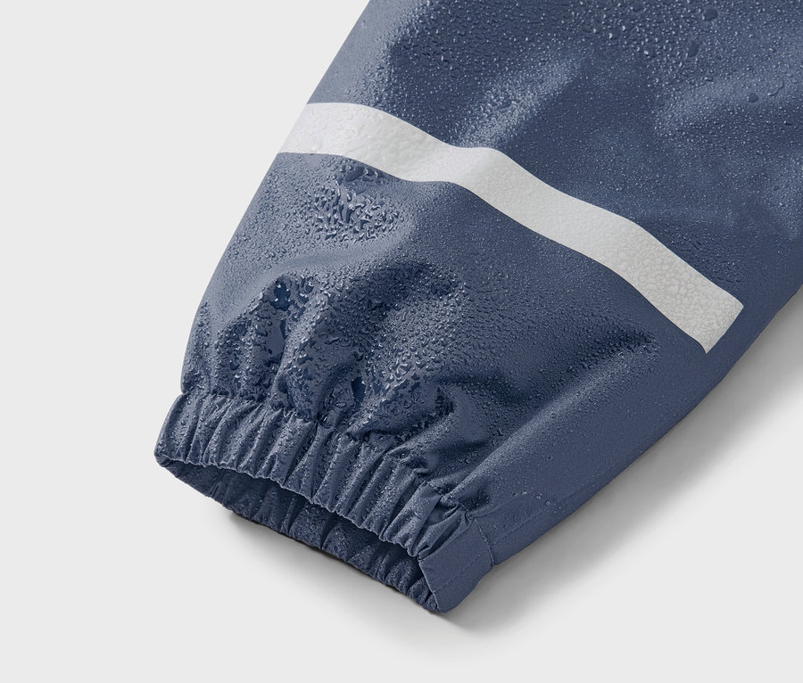 Gros plan sur la manche bleue d'une veste avec une bande blanche et des gouttes d'eau.