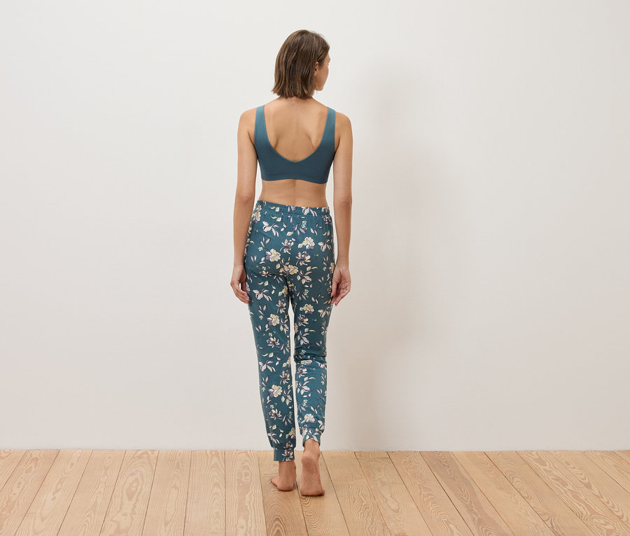 Vue arrière d'une femme portant un soutien-gorge de sport bleu et un pantalon fleuri sur un plancher en bois.