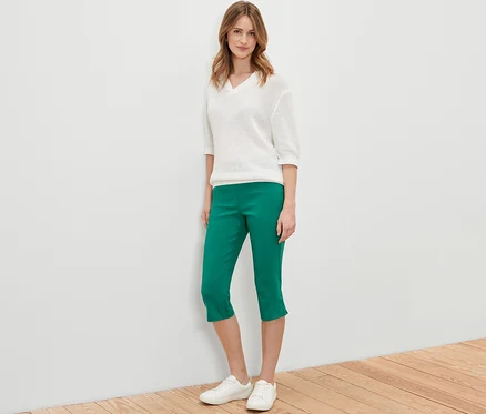 Femme posant en pantalon 3/4 en bengaline vert, pull blanc et chaussures blanches.