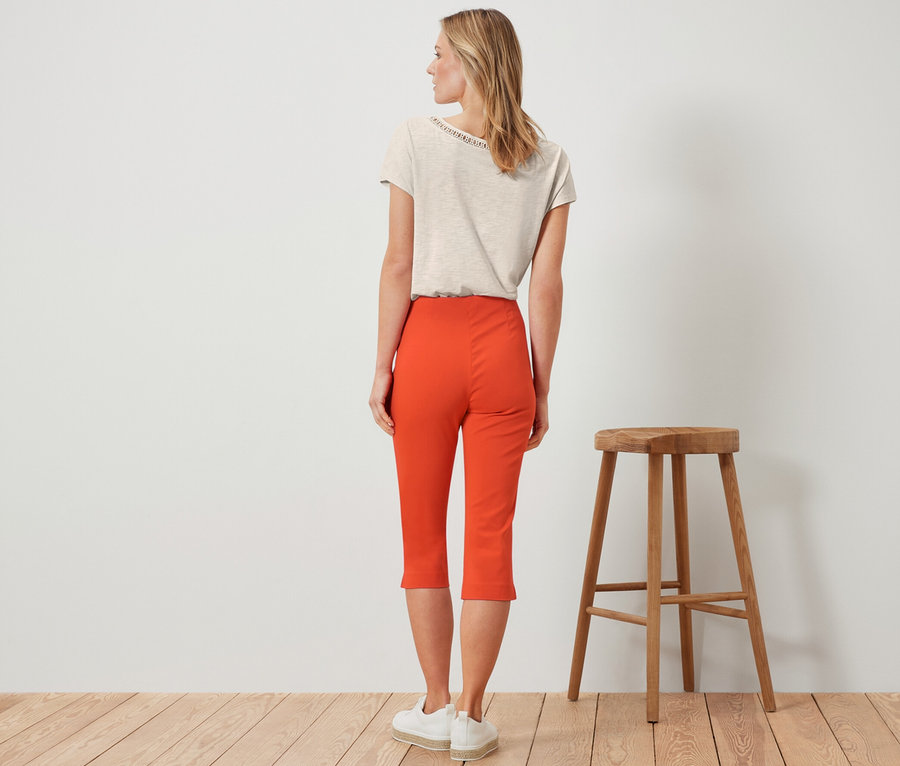 Femme debout de dos, portant un pantalon 3/4 stretch orange.