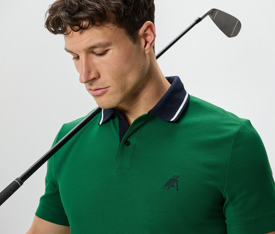 Un homme avec un club de golf sur l'épaule porte un polo fonctionnel vert.