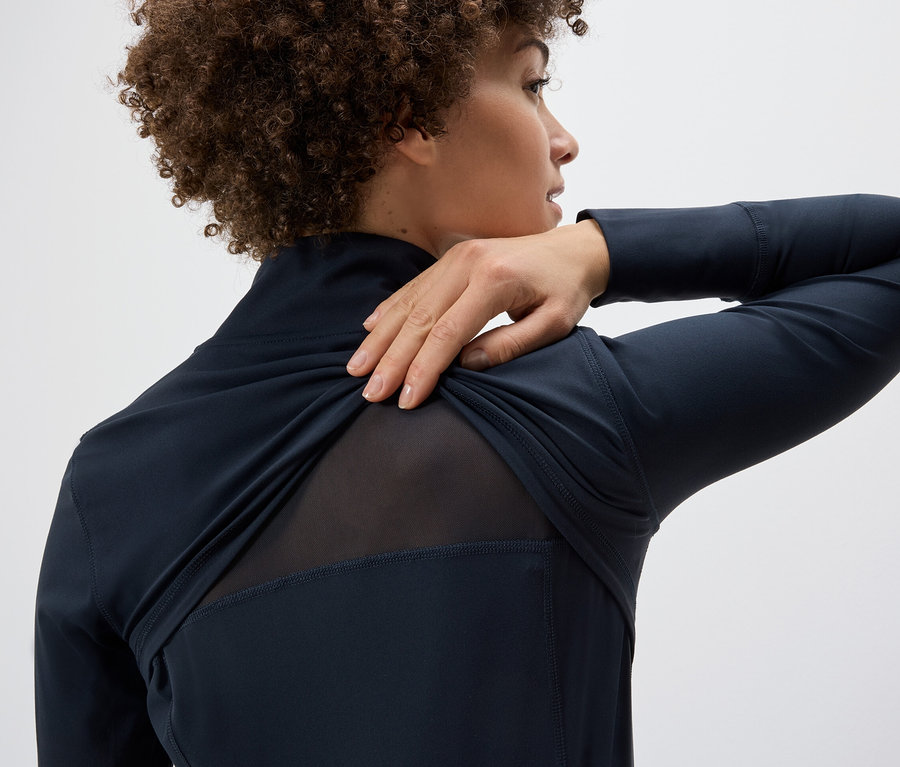 Femme tirant une veste fonctionnelle sur son épaule, révélant un empiècement en maille au dos.