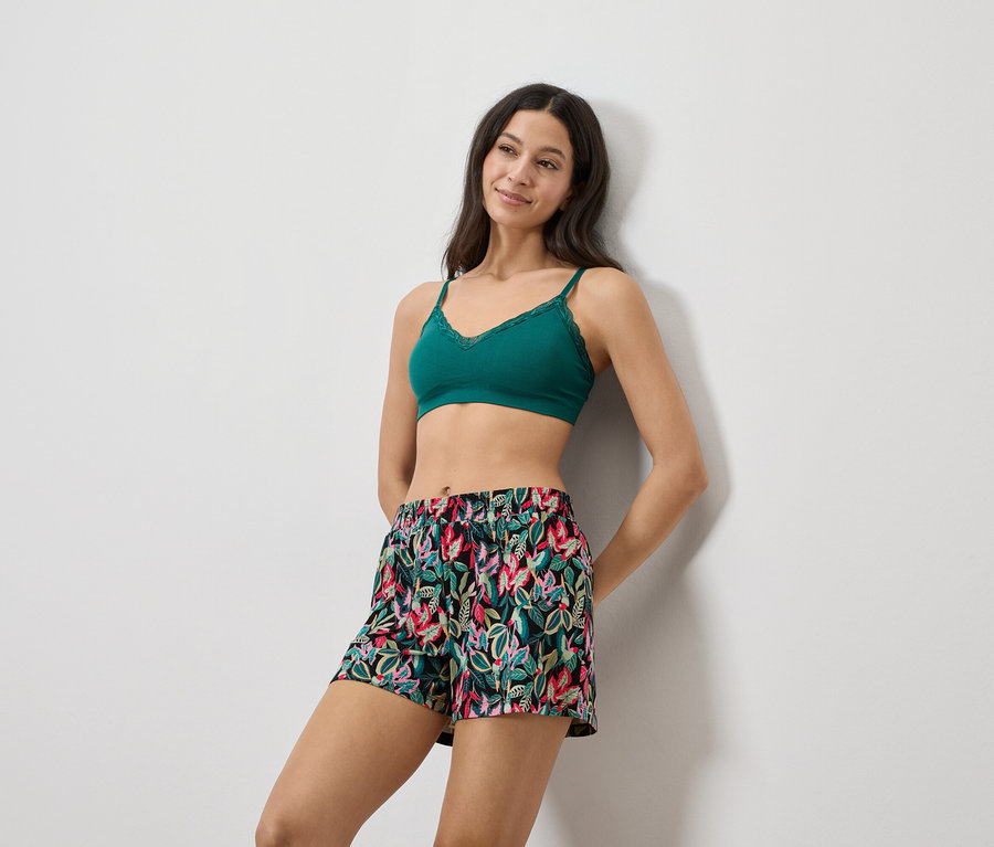 Femme appuyée contre un mur, portant une brassière en dentelle verte et un short à imprimé floral.