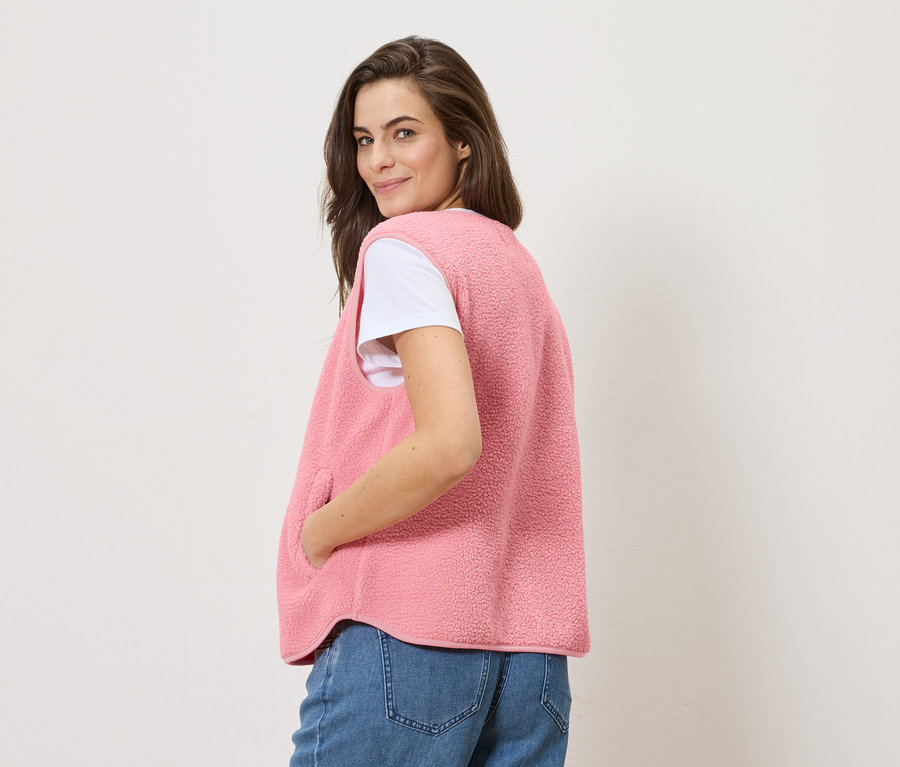 Une femme regarde par-dessus son épaule et porte un gilet sans manches en peluche teddy sur un t-shirt blanc et un jean.