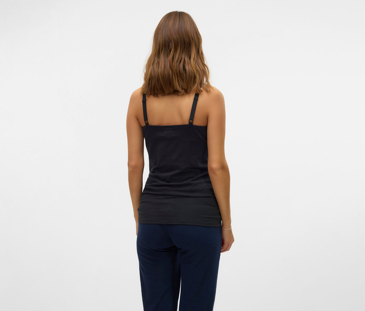 Femme vue de dos portant un des 2 tops à bretelles spaghetti noirs MAMALICIOUS «MLKERRIE» et un pantalon bleu sur fond blanc.