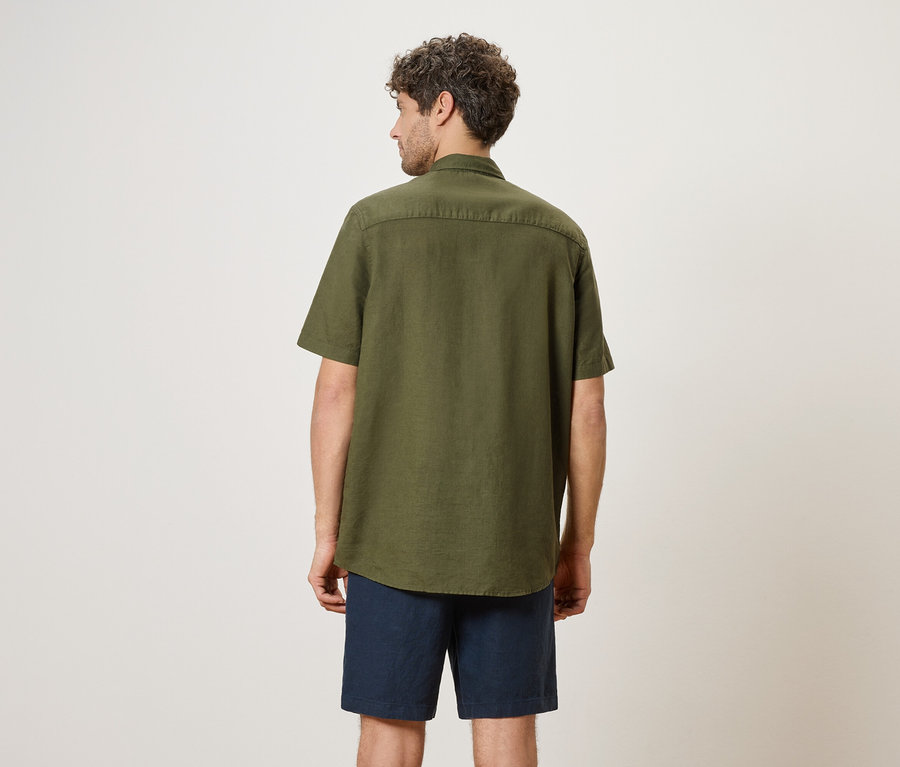 Un homme vu de dos, portant une chemise vert olive et un short bleu.