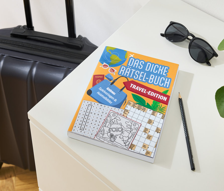 Une valise est posée à côté d'un livre de devinettes, de lunettes de soleil et d'un crayon sur une table.