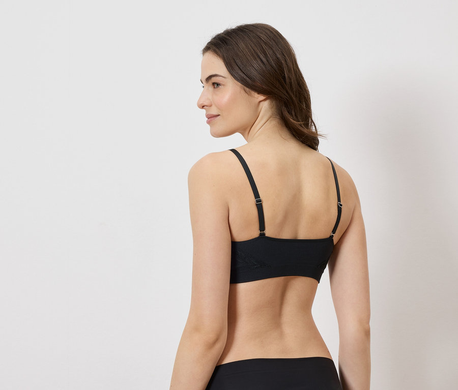 Femme vue de dos portant un soutien-gorge et une culotte noirs sur fond blanc.