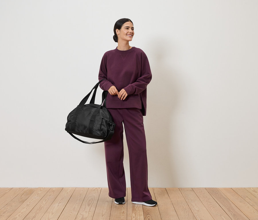 Femme en survêtement bordeaux tenant un sac de sport noir.