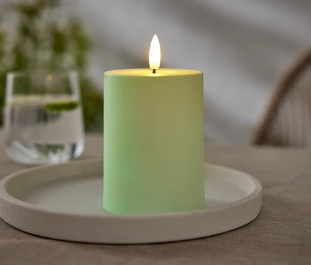 Une bougie verte est posée sur une assiette blanche. Un verre d'eau avec du citron vert est visible en arrière-plan.