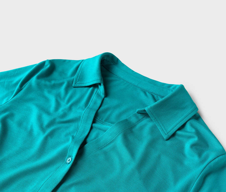 Gros plan d'une chemise turquoise avec col et boutons sur fond blanc.