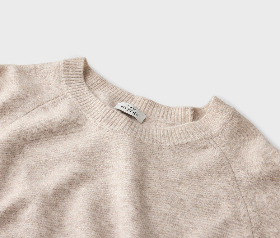 Gros plan d'un pull beige à col rond avec une étiquette indiquant « TCHIBO MY STYLE ».