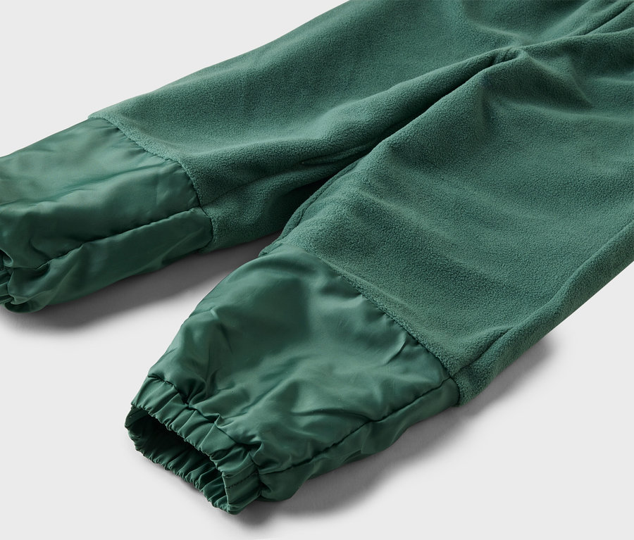 Gros plan d'un pantalon de jogging vert avec un haut en polaire et un bas brillant et froncé sur un fond gris.