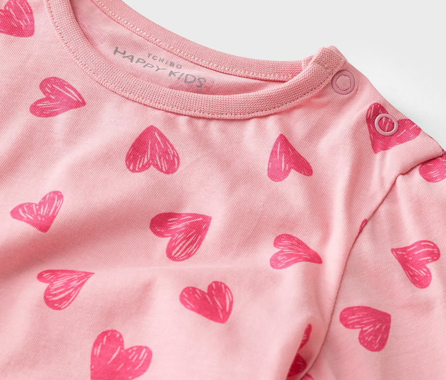 Gros plan sur un t-shirt rose à manches longues avec un motif de cœurs et des boutons-pression au col.