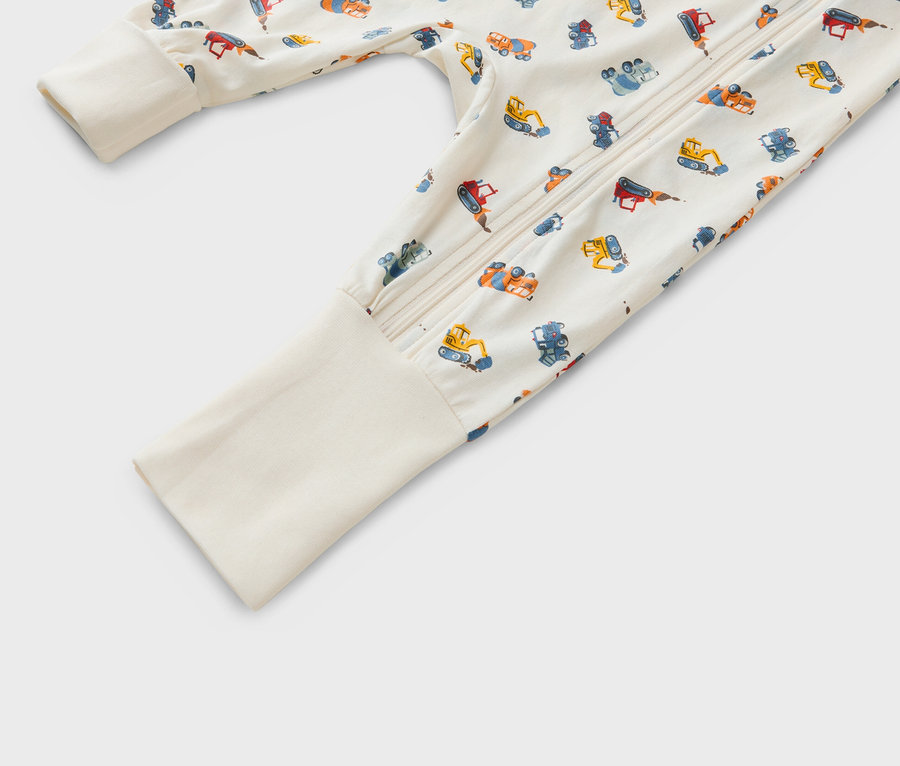 Gros plan sur un pyjama de bébé à fermeture éclair avec un motif de différents véhicules de construction sur un fond beige.