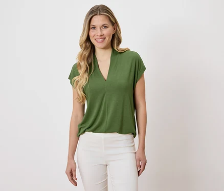 Femme portant un chemisier vert et un pantalon blanc.