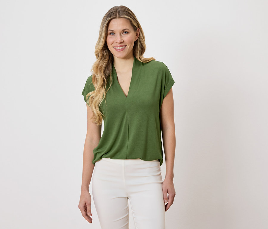 Femme portant un chemisier vert et un pantalon blanc.