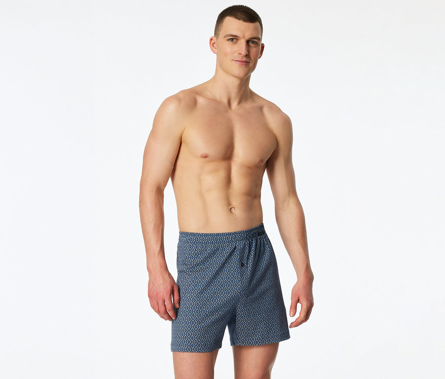 Un homme torse nu porte un boxer en jersey SCHIESSER bleu à motif losanges.