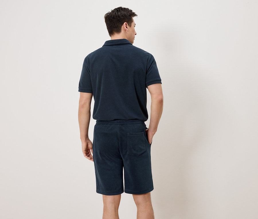 Un homme vu de dos portant un polo bleu marine et un short.