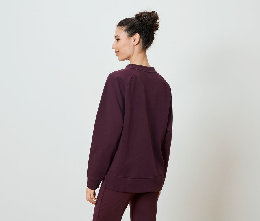 Femme vue de dos portant un pull bordeaux et un pantalon assorti.