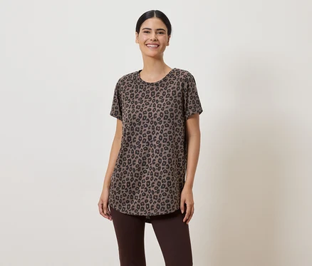 Une femme aux cheveux relevés porte un t-shirt marron à motif léopard et un legging marron sur un fond clair.